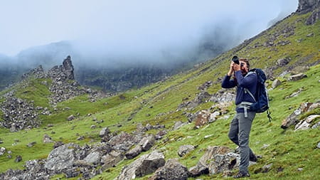 A man wearing a backpack and hiking boots takes a picture of the Scottish Highlands